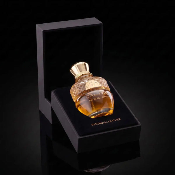 A bottle of Patchouli Leather Parfum with amber liquid and a gold cap, displayed in an open black presentation box on a glossy black surface.