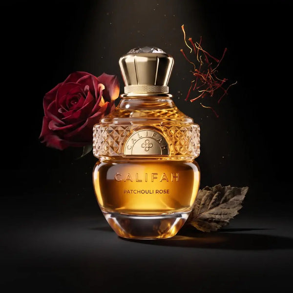 A bottle of CALIFAH Patchouli Rose Parfum with golden amber liquid, a textured gold neck, and a polished cap, styled with a red rose and a dried leaf on a black background.