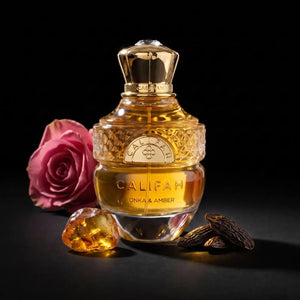 A bottle of CALIFAH Tonka & Amber Parfum with a gold cap and golden liquid, styled with a pink rose, a faceted amber gem, and whole almonds on a black background.