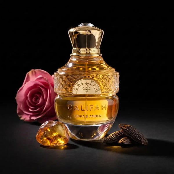 A bottle of CALIFAH Tonka & Amber Parfum with a gold cap and golden liquid, styled with a pink rose, a faceted amber gem, and whole almonds on a black background.