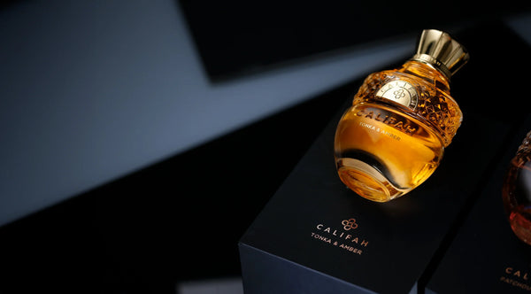 A bottle of Califah Tonka & Amber Parfum with amber liquid and a gold cap, displayed on top of its black packaging box.